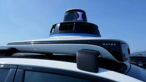 Waymo autonomous vehicle roof with a circular lidar sensor dome and side camera unit under a clear blue sky